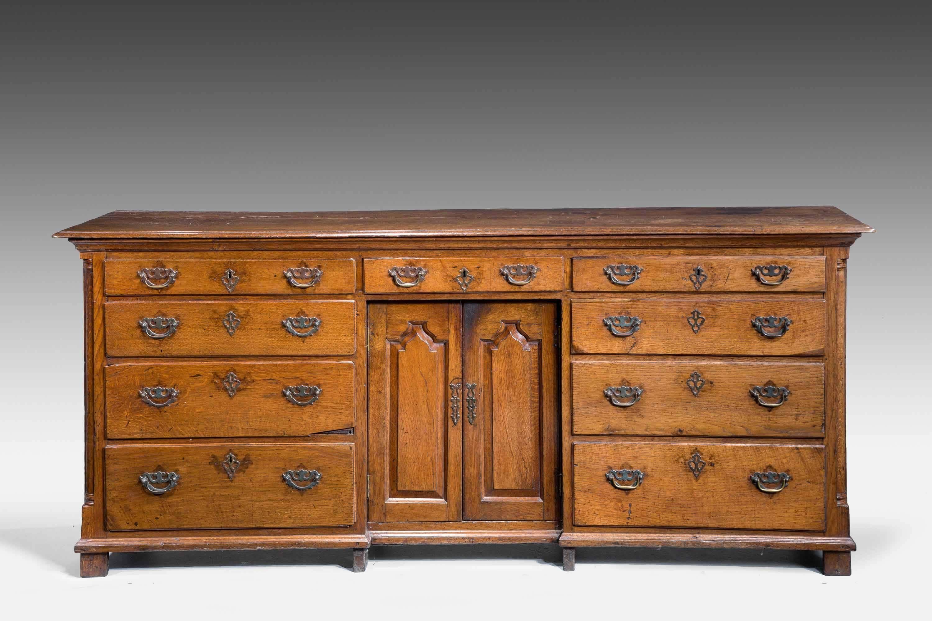 Good George III period oak dresser base incorporating a recess within a pair of panelled doors, nine graduated drawers to the front, the top patched during the 19th century. Strong overall design.

A Welsh dresser sometimes known as a kitchen
