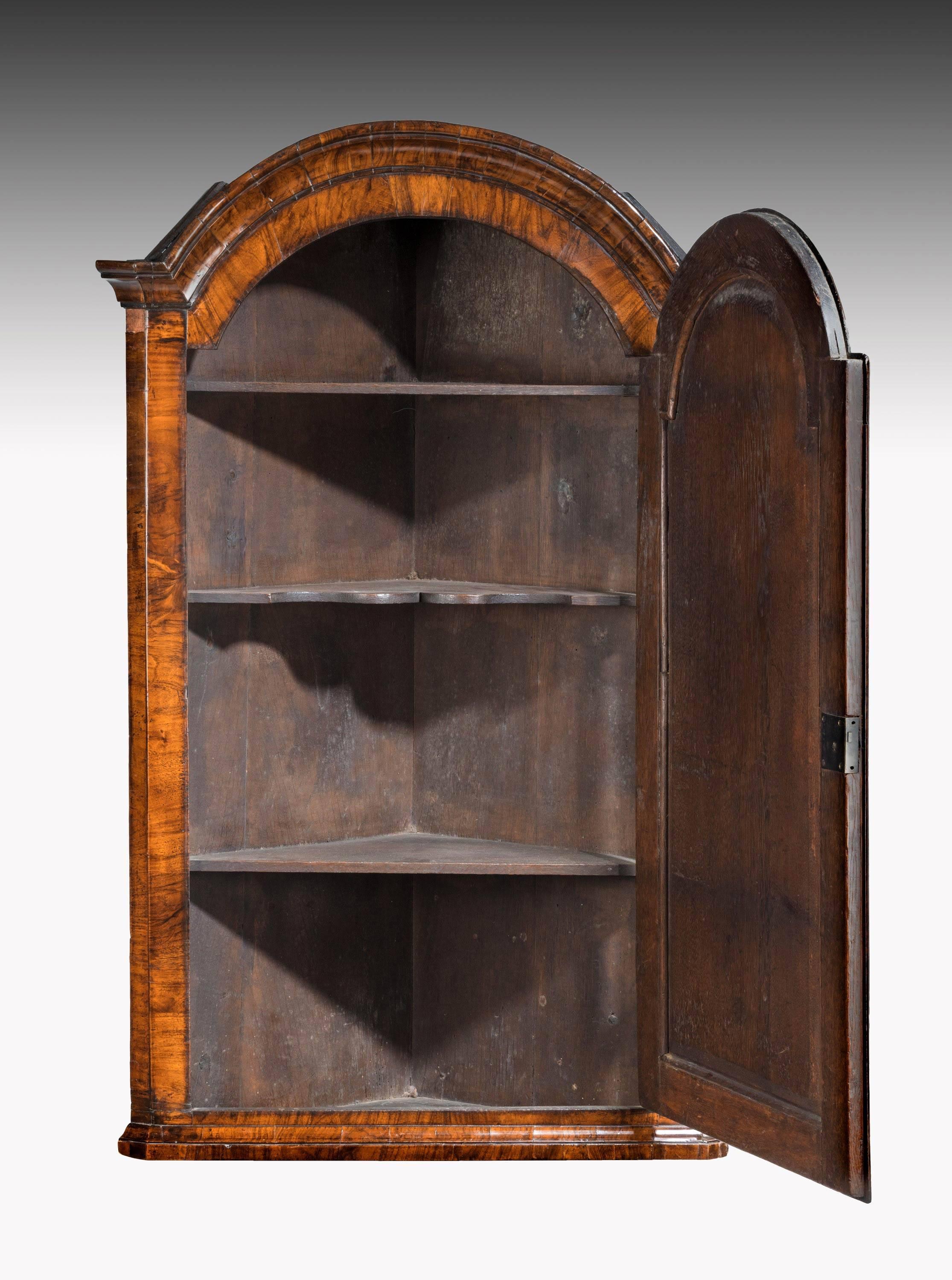 A very finely figured Queen Anne walnut corner cupboard. The domed top with corvetto mouldings over a crossbanded door.