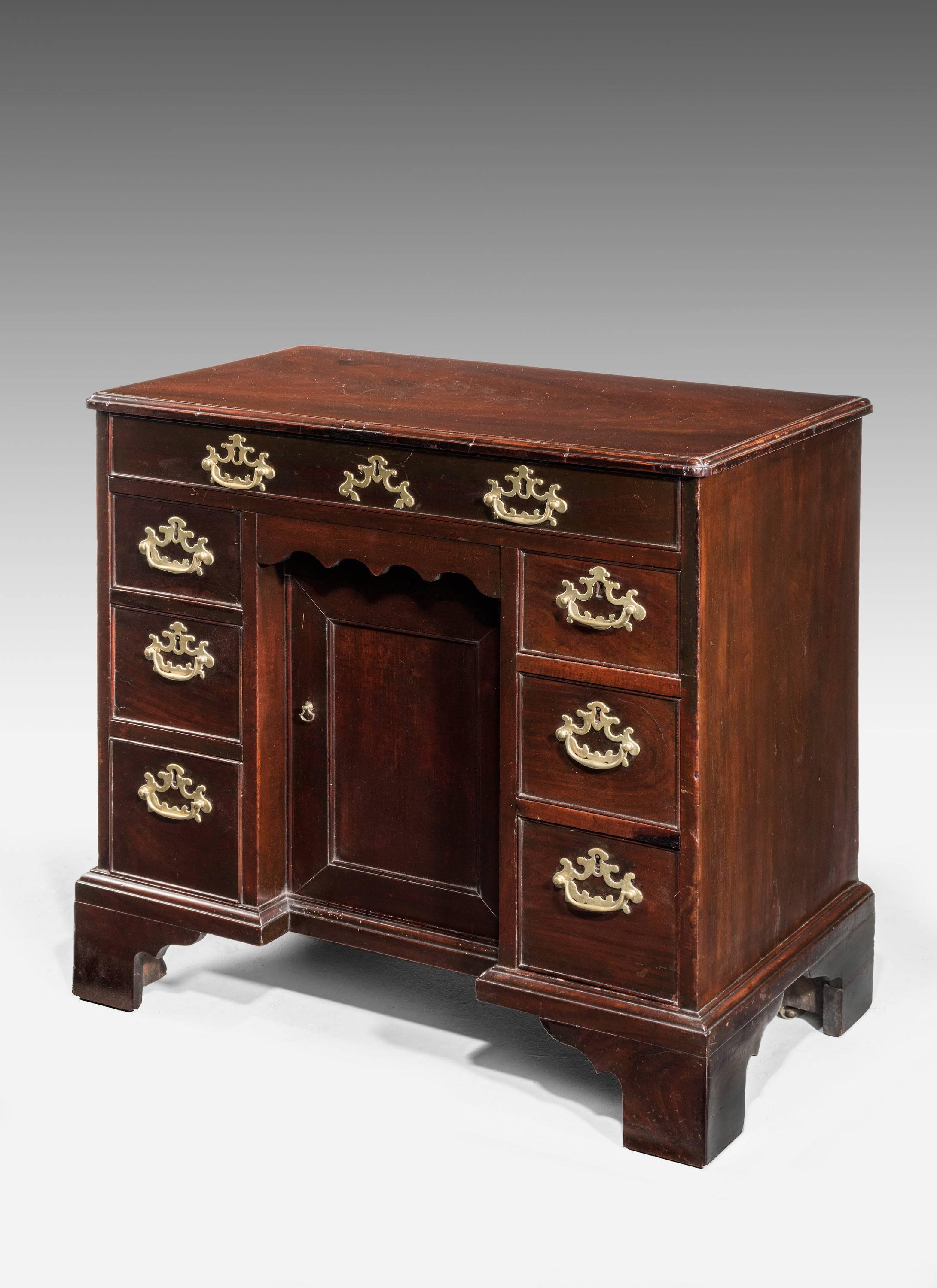 An unusually small and charming George II period kneehole desk. The cusb corners to the top over seven drawers and a centre cupboard. With original period bracket feet. Lovely pierced brass work. The whole very well formed and of excellent