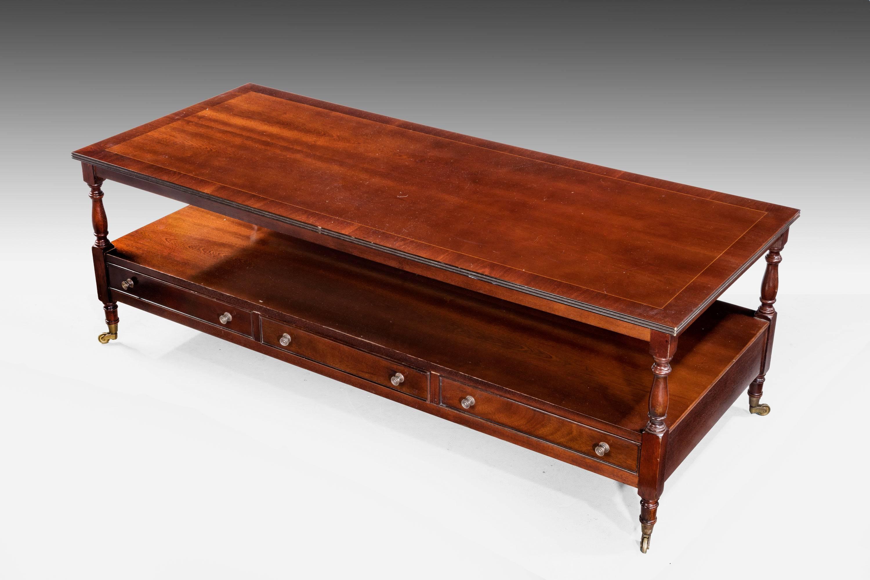 A mid-20th century low rectangular table, the top cross banded in mahogany with line inlay. The base incorporating three drawers on turned supports and with original shoes and casters.


