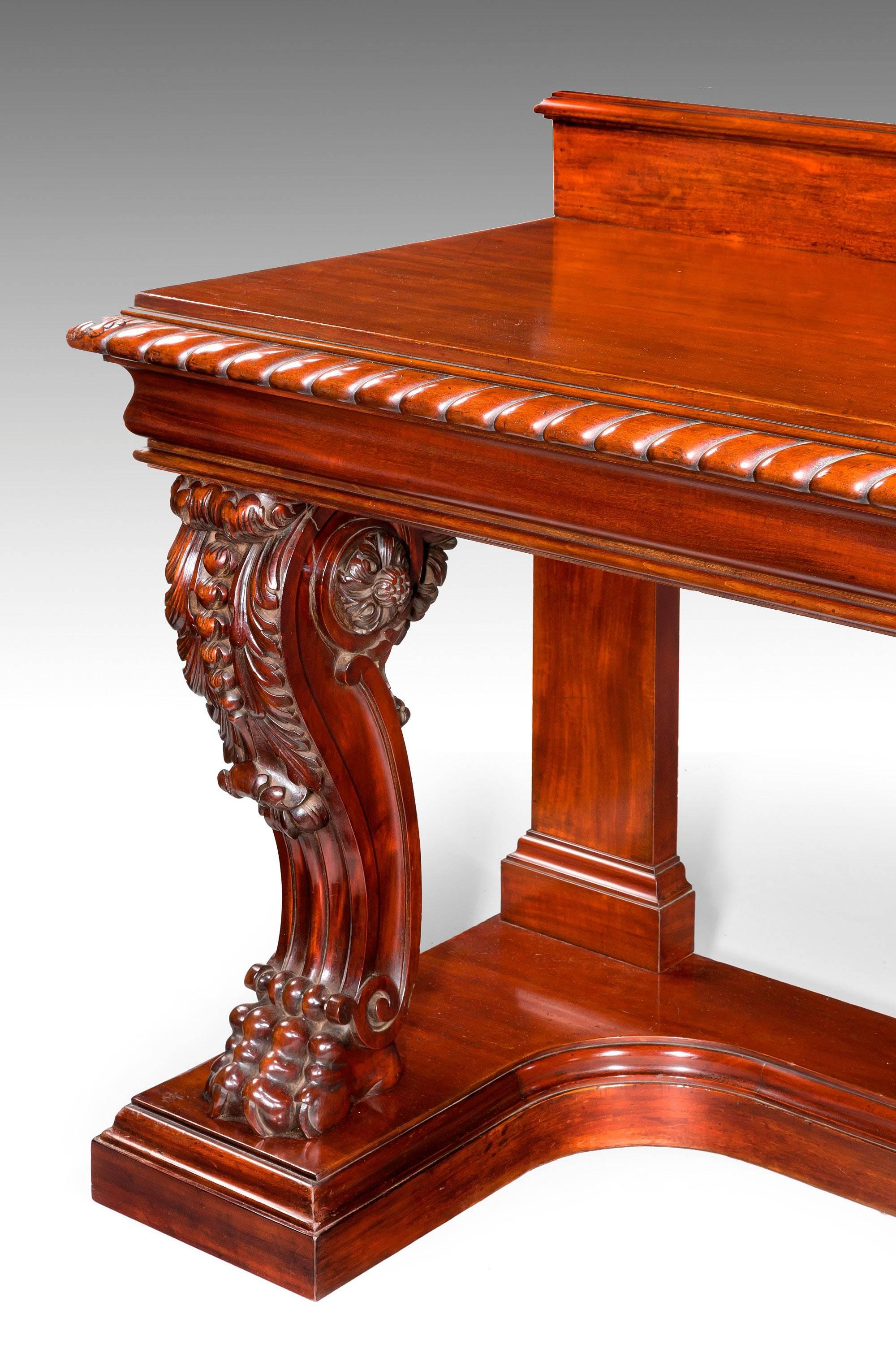 A Regency period serving table on a raised platform. The continuous carved upper border with acanthus leaves at each terminal over two superbly designed and carved supports, strongly scrolled cabriole design with patera to the shoulders and