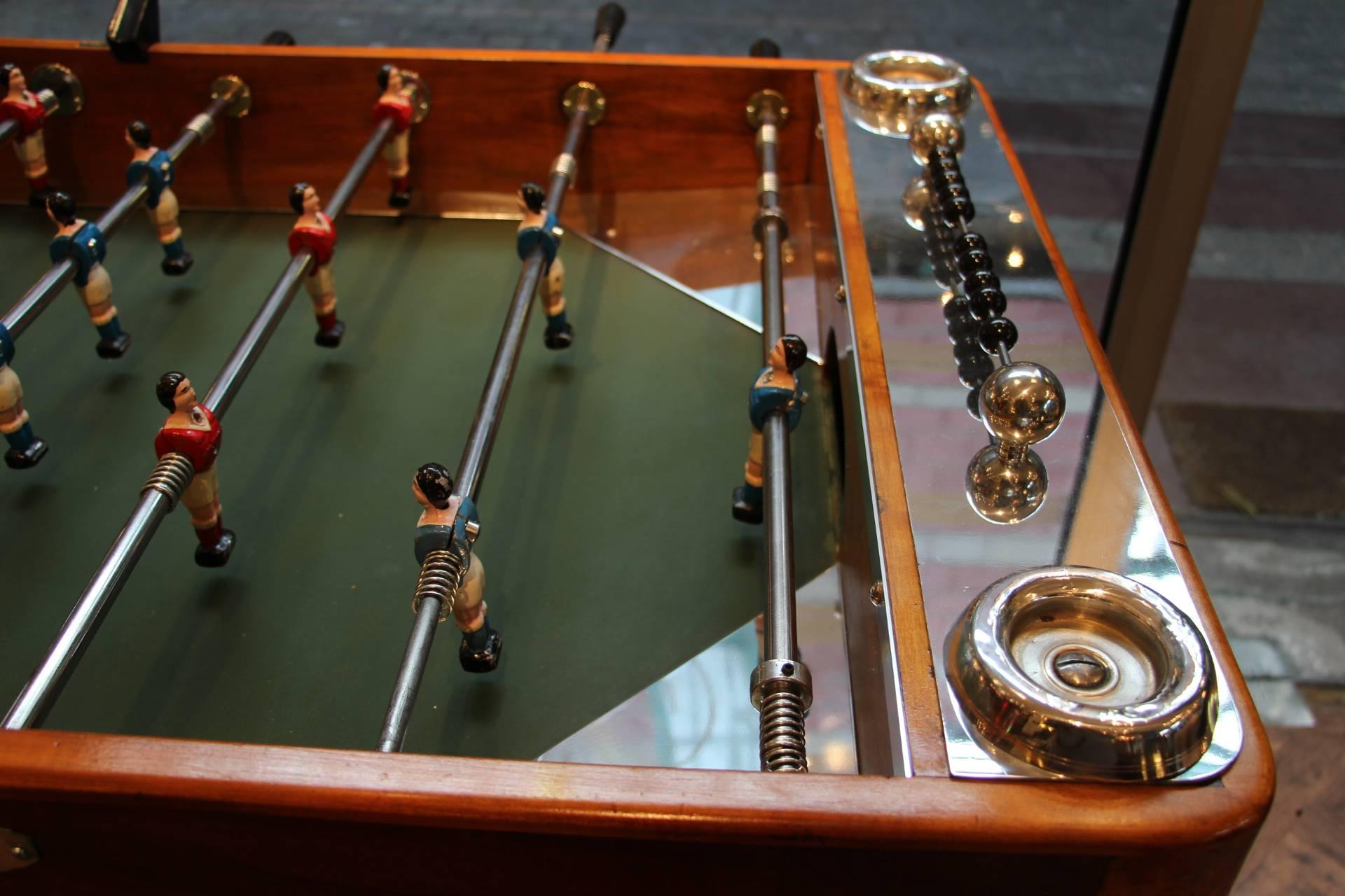 This foosball table is very unusual because it features a honey color burr walnut. It still has got its four original ashtrays, as well as all its polished aluminum pieces. Its players are red and blue and the original green field is made of glass.