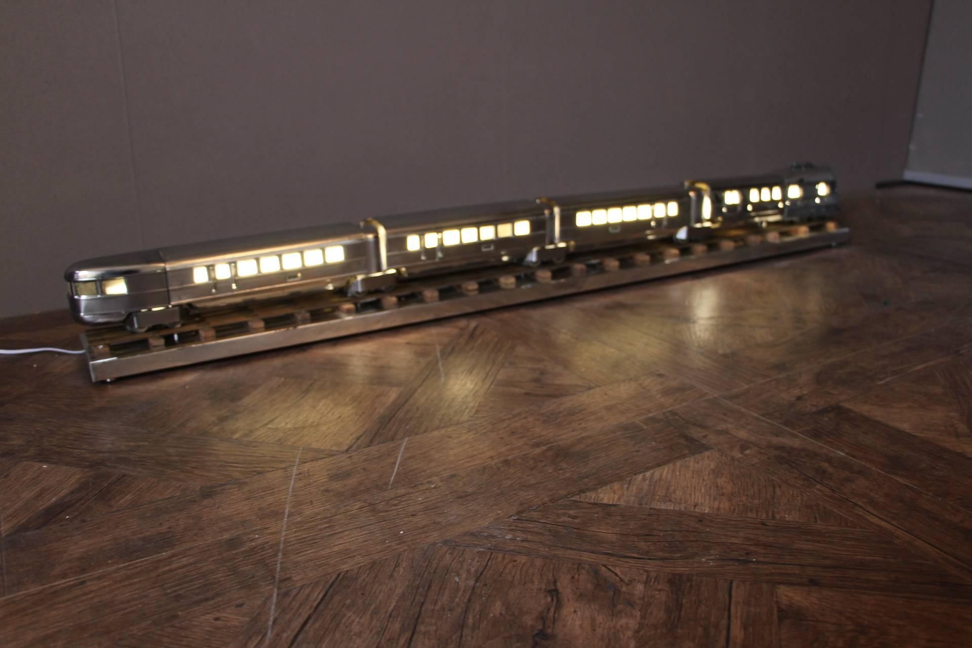 This polished aluminium train is fitted with LED lights inside and makes a spectacular and beautiful lamp.
It is a very unusual piece that can be placed in an office, a living room or even in a bedroom.
It is fixed on its polished aluminium Stand