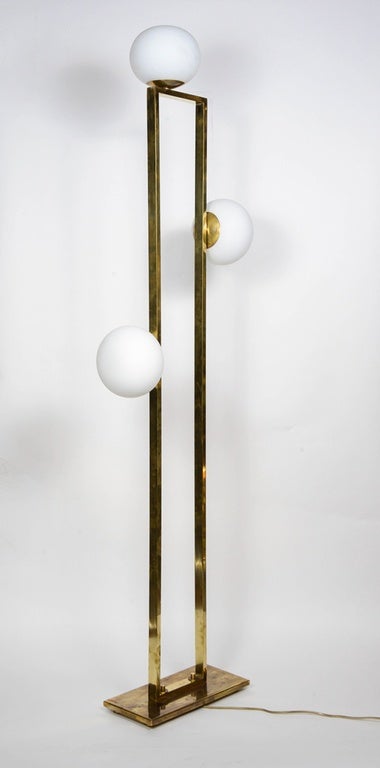 Pair of elegant floor lamps made of brass, each with three white glass globes.

New design by Glustin Luminaires.