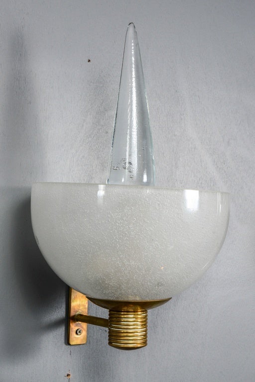 Particular and unusual 1960s set of four wall sconces. Made of a brass structure holding a thick Murano glass half sphere hiding the two sources of light. From the sphere a vertical glass spike is rising.
