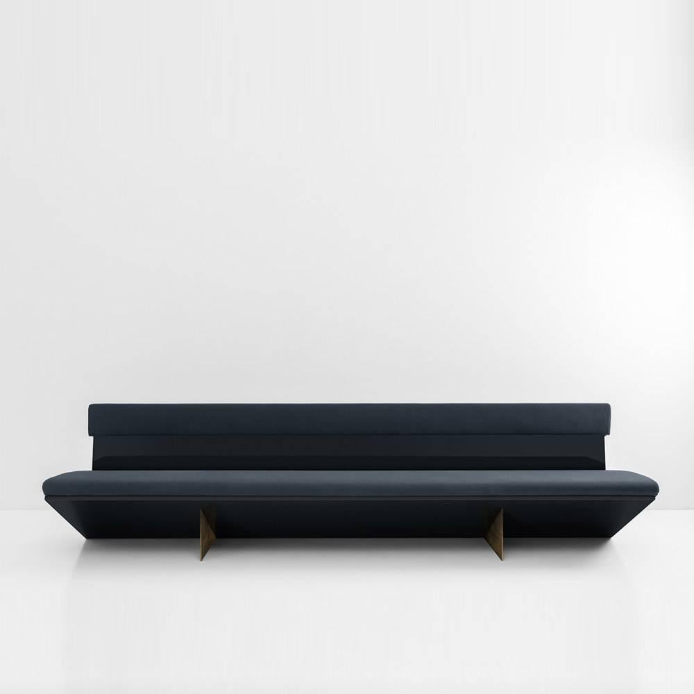 Low slung and architectural, this sofa features a curved structure made from glossy lacquered wood and legs made in oxidized brass. The cushion is padded with polyurethane foam and upholstered in fabric by DIMORESTUDIO or with your choice of fabric.