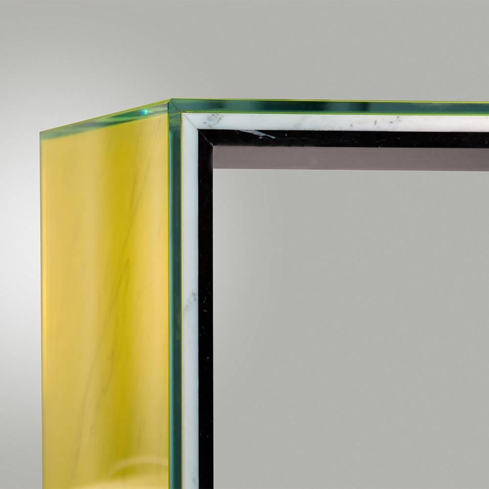 A layer of white Carrara marble, black nero marquina marble and acid yellow tinted glass are sandwiched together to form this modern, sculptural console table. The veins of the Carrara marble are visible through the glass allowing the marble to