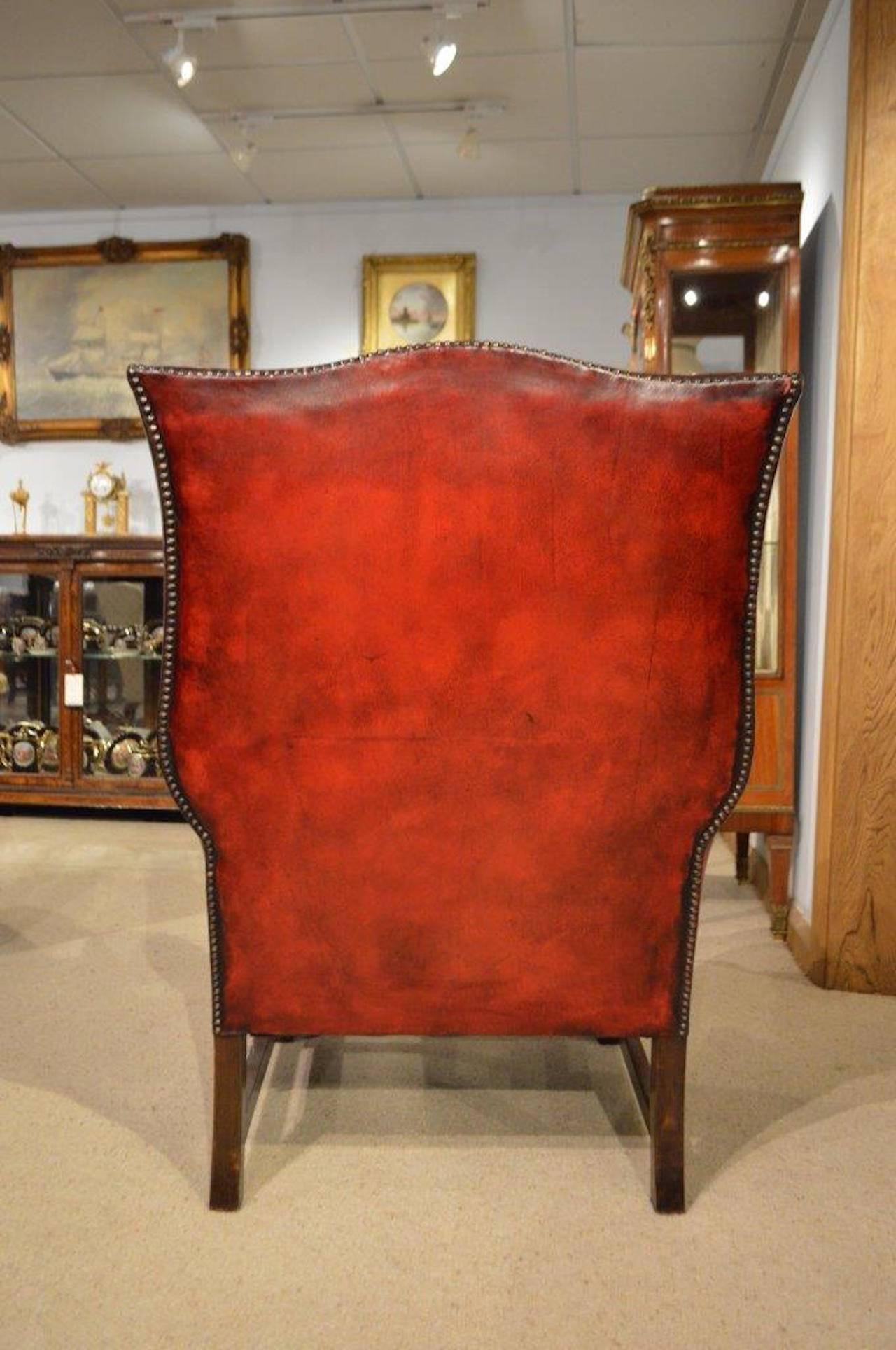 A good oak and red leather Edwardian Period antique wing armchair. Of traditional form the padded back, winged sides and rolled arms upholstered in high quality red leather with brass studded detail. Supported on Jacobean style oak turned supports