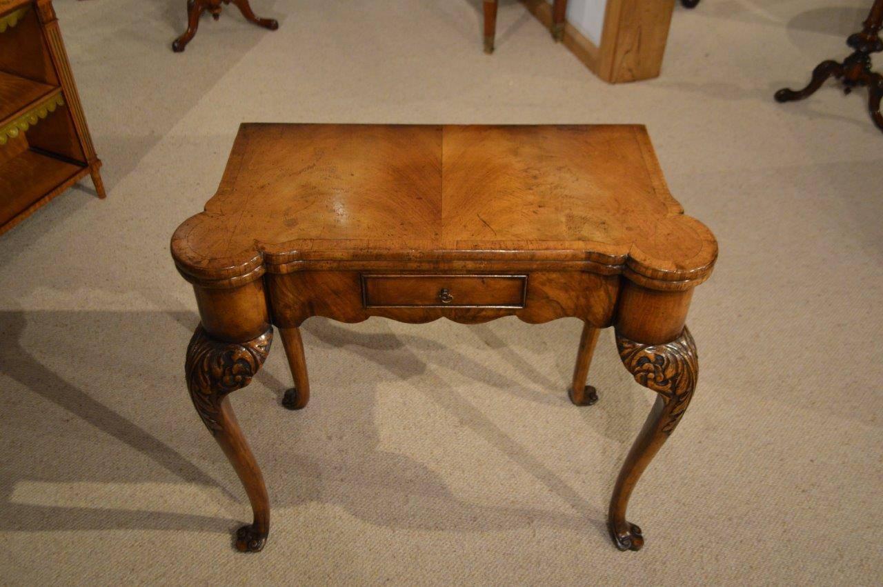 A walnut George I Style antique card table. Having a shaped top veneered in figured walnut with walnut banding and opening to reveal a baize lined playing surface with circular counter wells to each corner. The top whilst open is raised on a