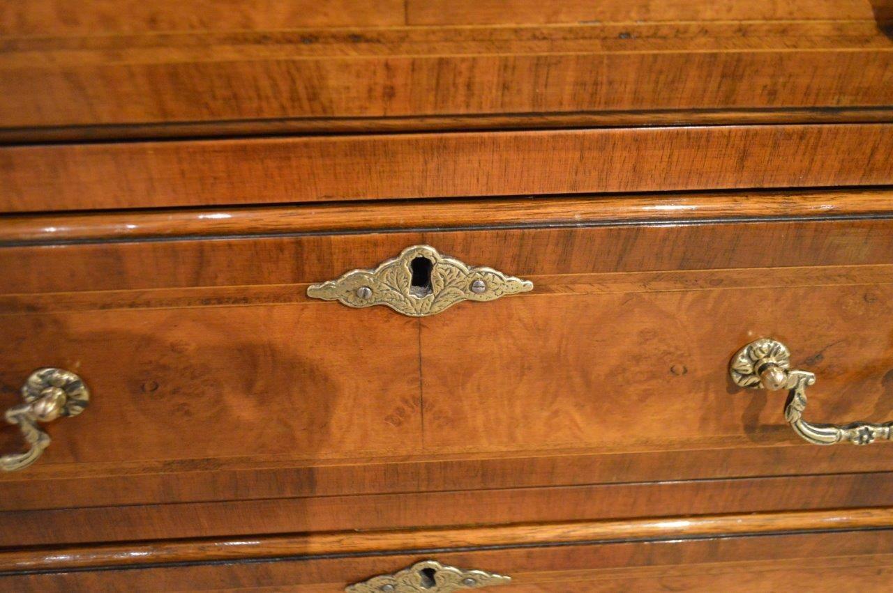 A burr walnut and herringbone banded George I style bachelors chest. The rectangular hinged top veneered in burr walnut with herringbone banded detail above an arrangement of four rectangular oak lined drawers, each having period style brass handles