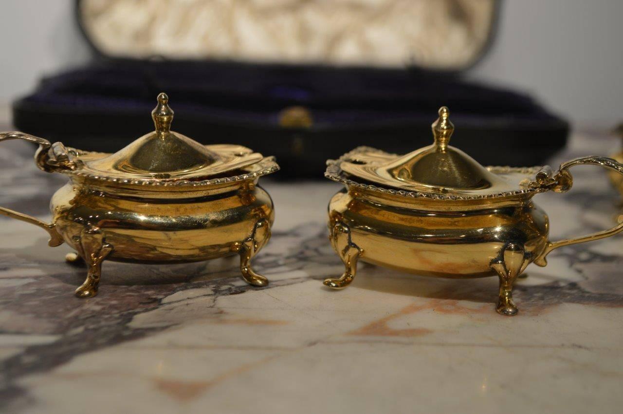 A silver gilt Edwardian period six-piece condiment set comprising of two pepper pots, two salt cellars with the original blue glass liners and two mustard pots with serving spoons. Hallmarked Birmingham 1910 and housed in the original velvet lined