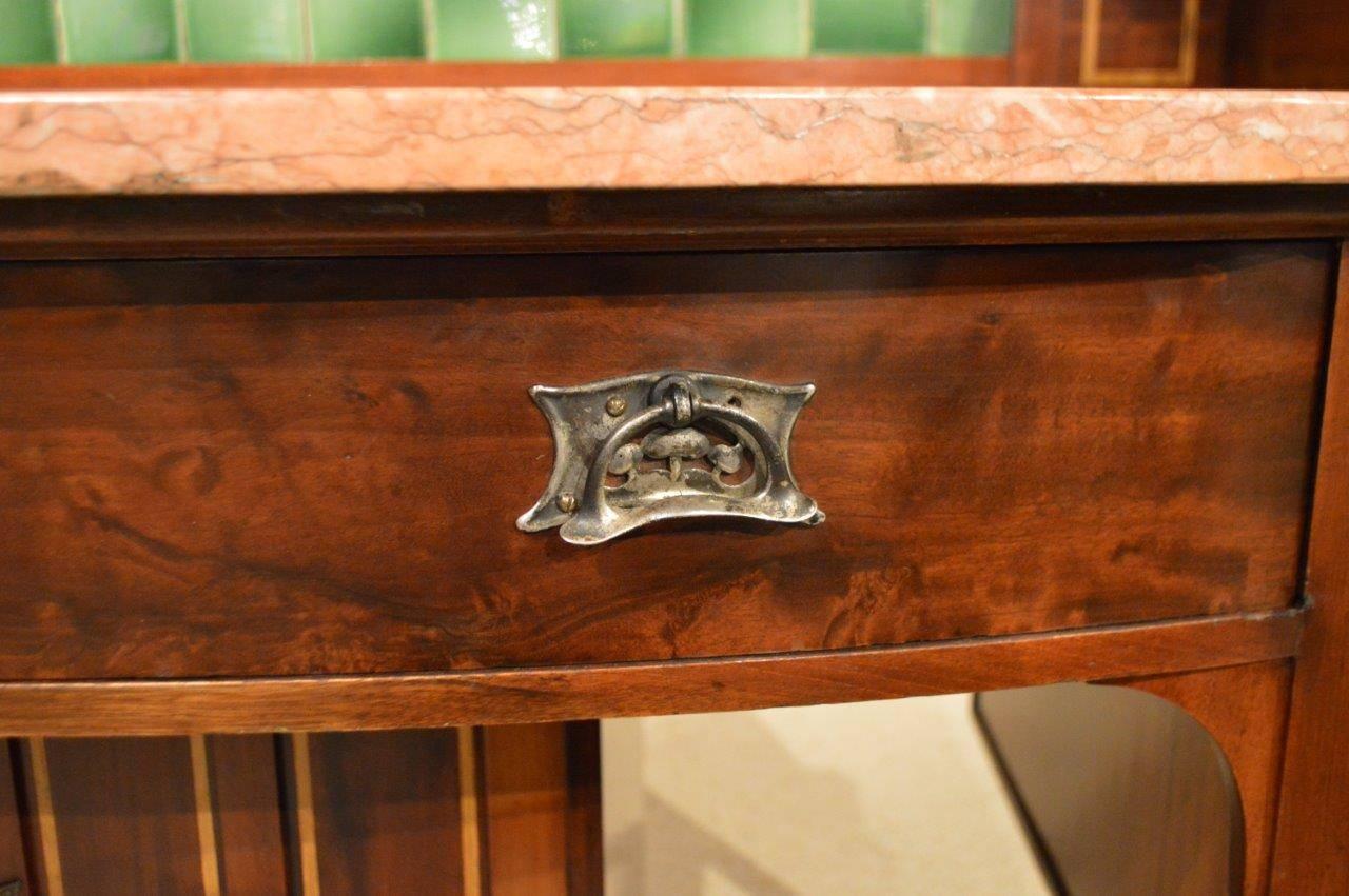 A mahogany inlaid Arts and Crafts period washstand by Shapland & Petter of Barnstaple. The raised tiled back with stylised Art Nouveau ceramic tiles, flanked by fine marquetry and mother-of-pearl inlaid panels, above a bow front mahogany frieze