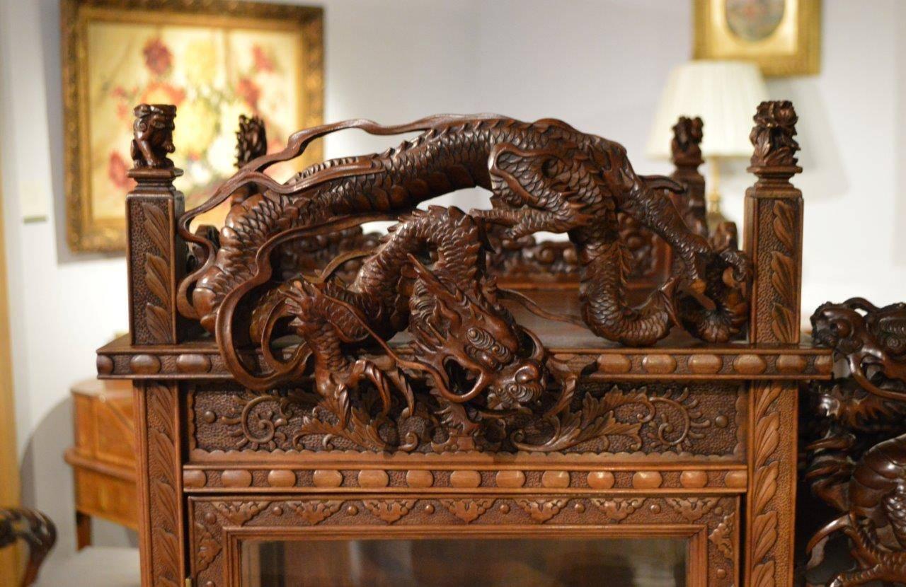 A carved cabinet on stand Japanese Meiji period. The upper section with finely carved chasing dragons and a carved cloud band frieze, terminating in finely carved finials. The two rectangular glazed doors opening to reveal a stepped shelved