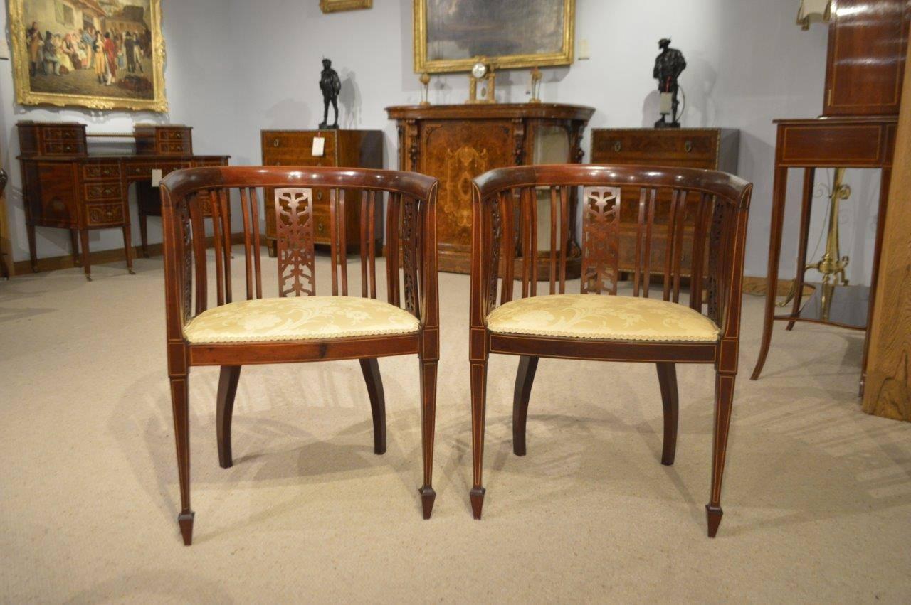 A pair of mahogany inlaid Edwardian period antique bedroom chairs. Each with a mahogany curved back with three pierced fretwork panels and further mahogany supports above a shaped padded seat. Supported on elegant square tapering supports with spade