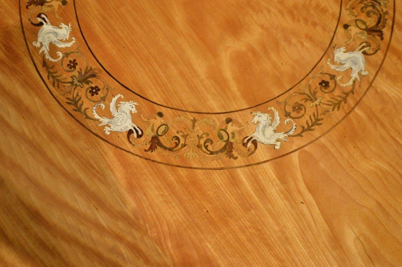 A circular satinwood and marquetry inlaid Victorian period antique occasional table. The circular satinwood top with a fine marquetry circular panel depicting griffins and Britannia with foliate inlaid detail and with a purple heart line inlaid