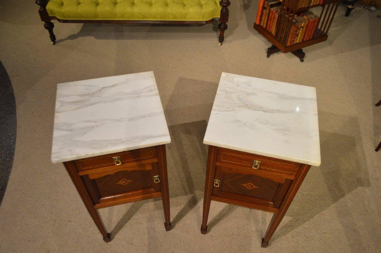 A good pair of mahogany inlaid French antique bedside cabinets. Each having a white veined marble top and with a rectangular oak lined drawer above a panelled door which opens to reveal a porcelain lined interior. Constructed using solid mahogany