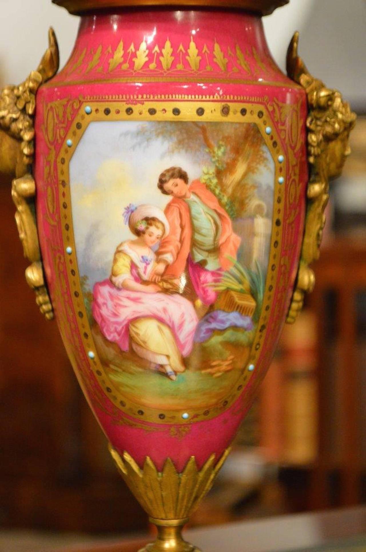 A pair of Sèvres style, late 19th century pink porcelain urns. Each with finely cast ormolu finials and satyrs. The porcelain bodies with fine hand-painted decoration depicting lovers and with applied jewelry detail. Raised on finely cast ormolu