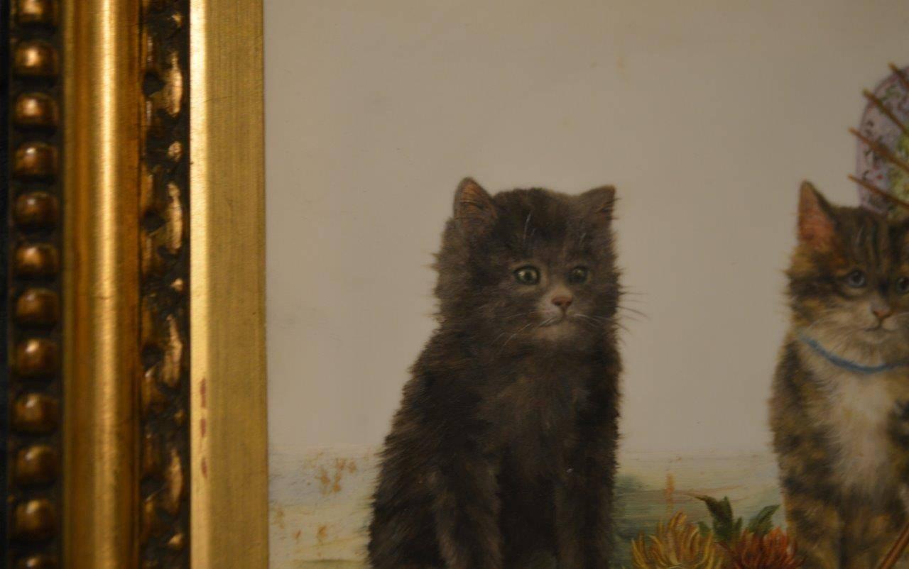 A small oil painting of kittens by Bessie Bamber depicting three kittens under an umbrella, painted on glass and with the 