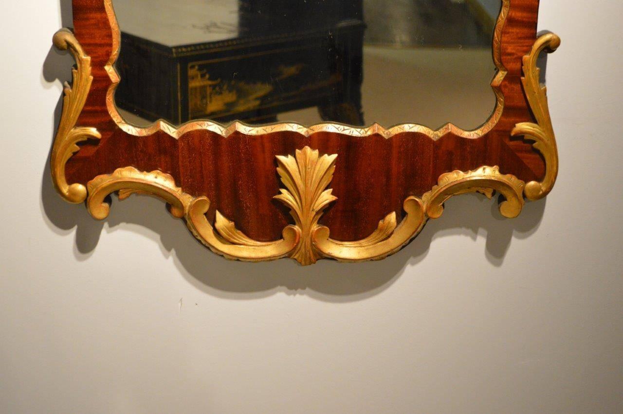 A mahogany and carved giltwood George II style wall mirror. Having a broken swan neck pediment with a carved giltwood phoenix above the mahogany veneered frame, housing the original shaped mirror and having carved giltwood mouldings, English, circa