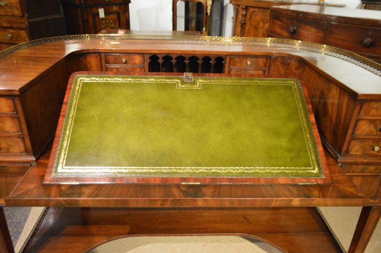 A fine quality George III style flamed mahogany Carlton House desk. The upper section with a pierced brass gallery and solid mahogany top above an arrangement of flame mahogany drawers, cupboards, pigeon holes and an adjustable green leather writing