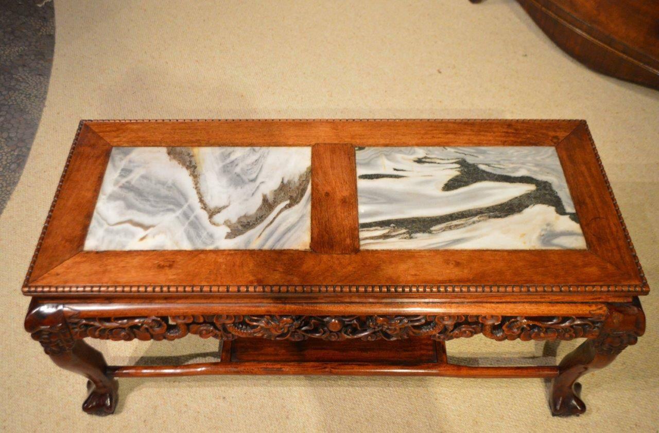 A Chinese hardwood marble inset coffee table. Having a solid rectangular top with twin rectangular inset moonstone marble panels, above a pierced border depicting chasing dragons. Supported on carved cabriole supports with claw feet united by an