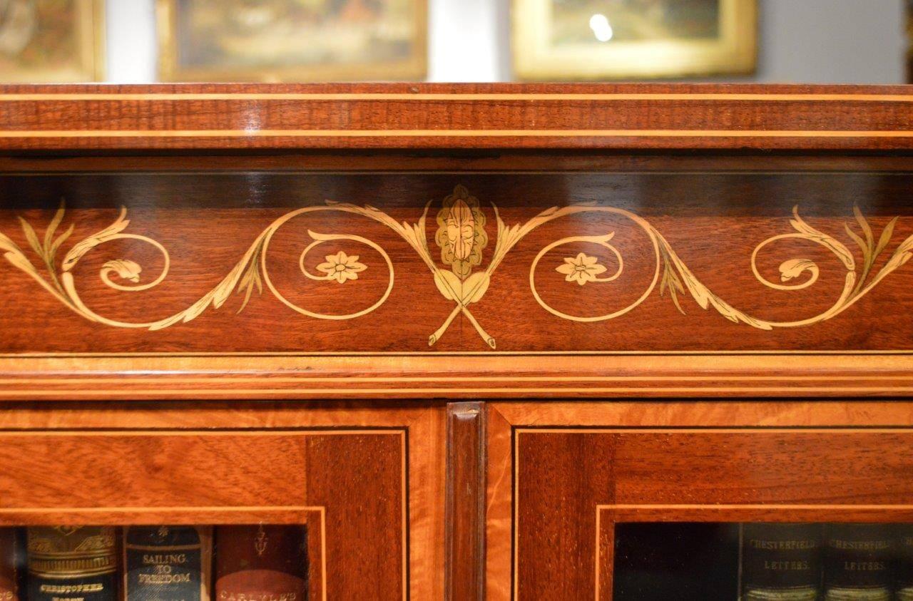A Fine quality marquetry inlaid Edwardian period two-door bookcase probably by Edwards & Roberts of London. Having a rectangular top made from plum pudding mahogany, banded in satinwood and with a Fine marquetry and pen-work inlaid panel with ribbon