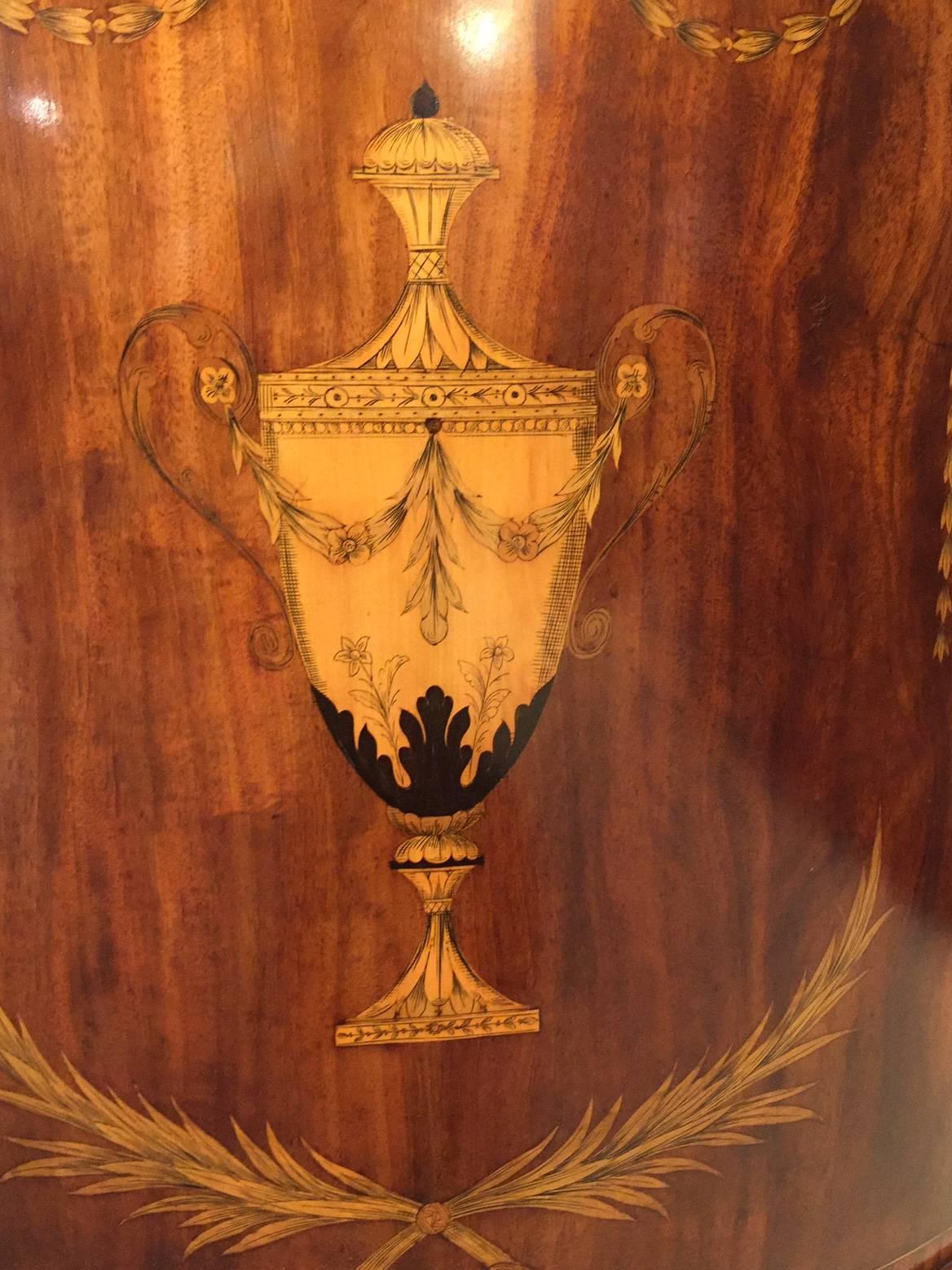 A mahogany inlaid Edwardian period Sheraton Revival corner cabinet. Having a triangular top with a classical Robert Adam designed marquetry urn with foliate and pen-work detail cross banded in kingwood above a ribbon and swag marquetry inlaid