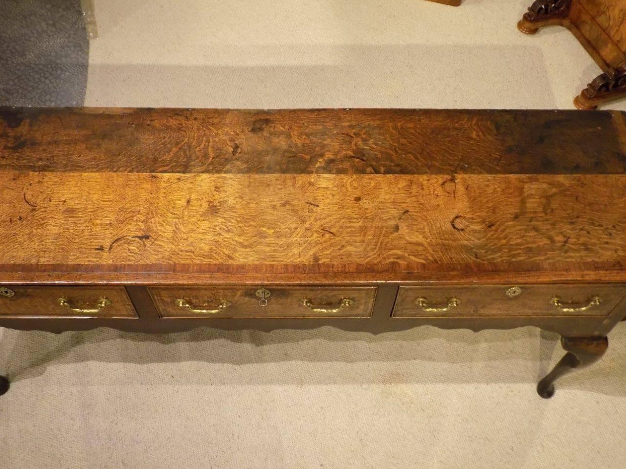 An oak George III period antique dresser base. Having a rectangular two plank top crossbanded in mahogany above three rectangular oak lined drawers with mahogany crossbanded detail and brass swan neck handles. With a wavy frieze and supported on