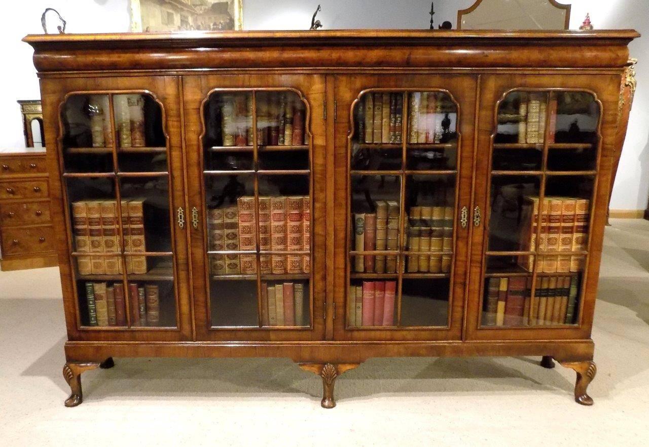 A beautiful walnut Queen Anne Revival four-door bookcase. Having a rectangular walnut top with cross grain moulding above a cushion moulded frieze and with four shaped walnut doors and further cross grain moulding, opening to reveal adjustable