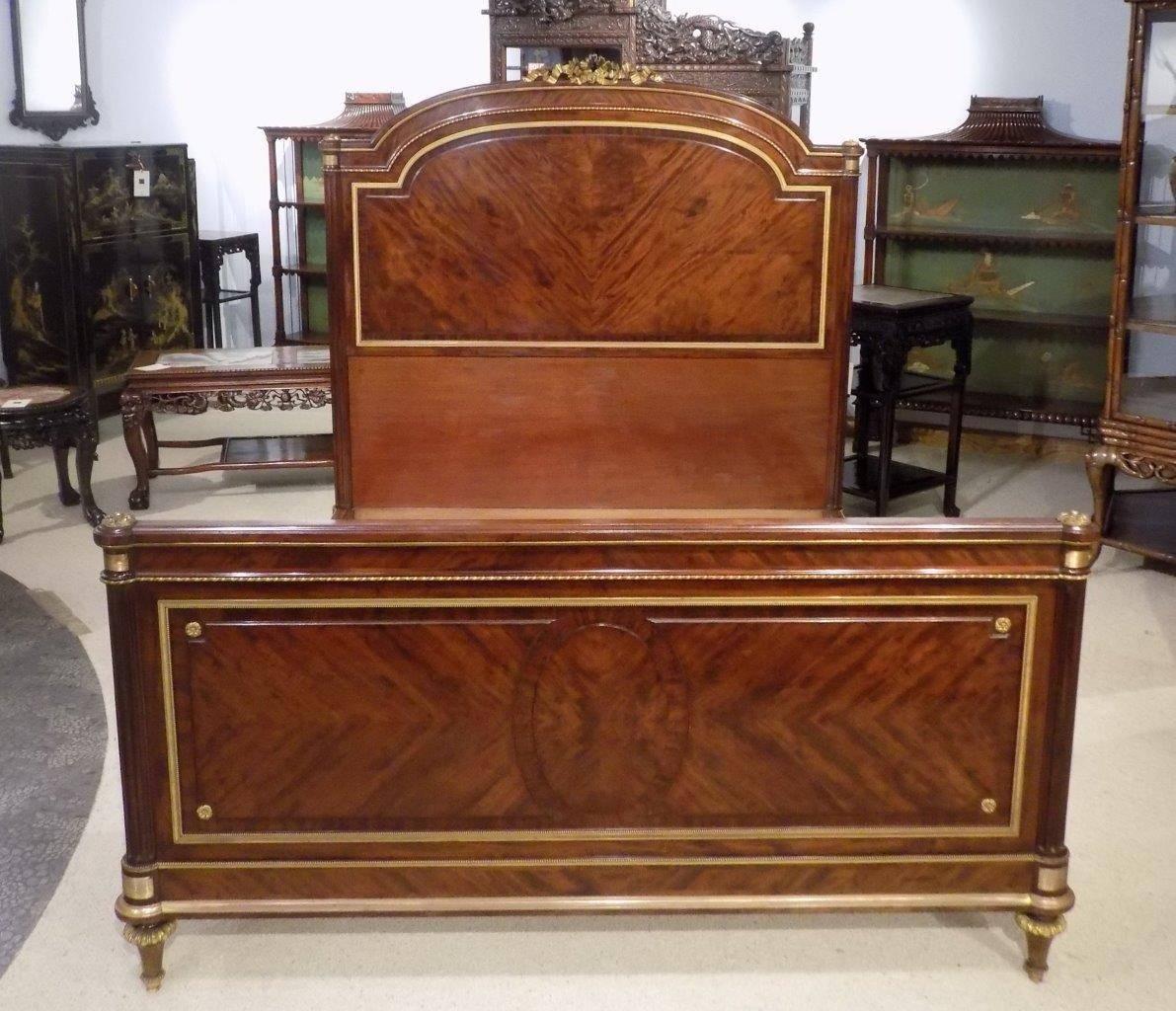 A superb French 19th century figured mahogany and ormolu-mounted antique king-size bed. The headboard having a finely cast ormolu ribbon and swag cartouche, above the central figured mahogany panel, with fluted column supports and fine quality cast