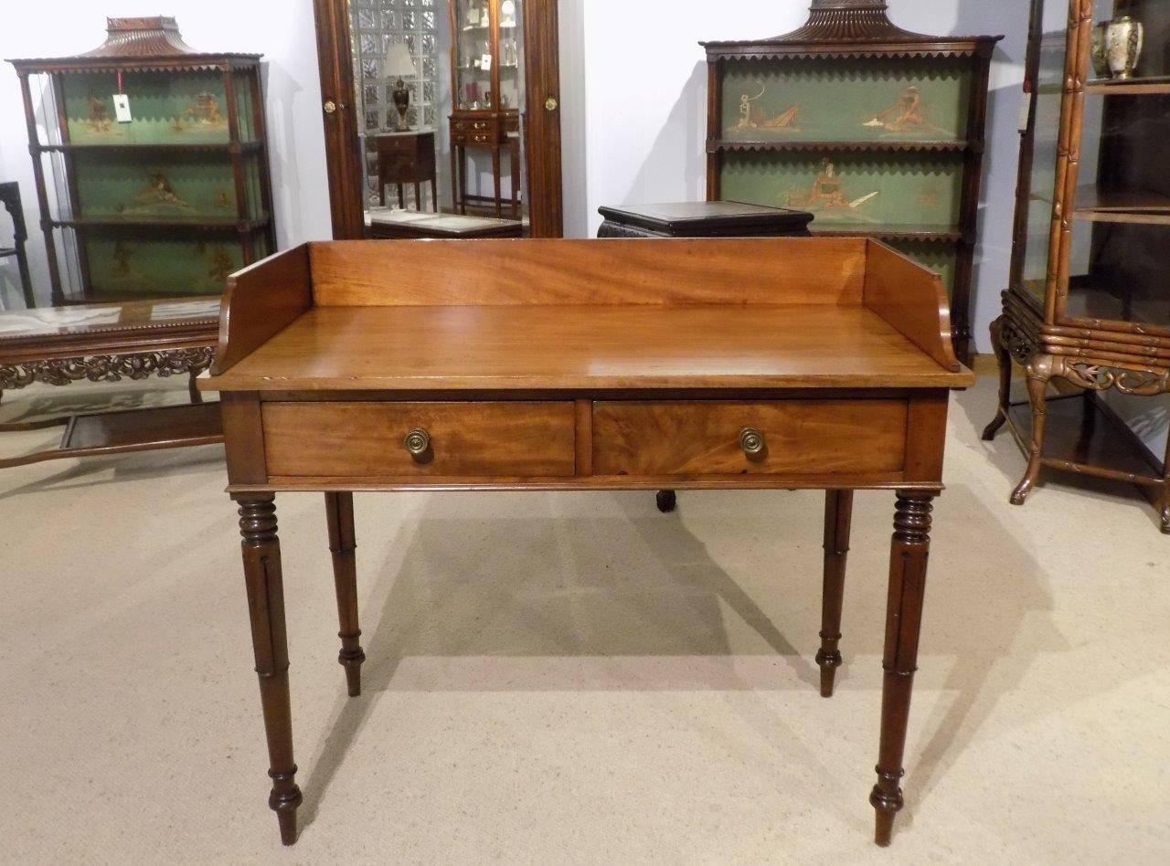 A mahogany William IV period two-drawer hall table. The raised galleried back above the solid mahogany rectangular top and with twin rectangular mahogany lined drawers with brass knobs. Supported on four turned and lappet carved legs, English, circa