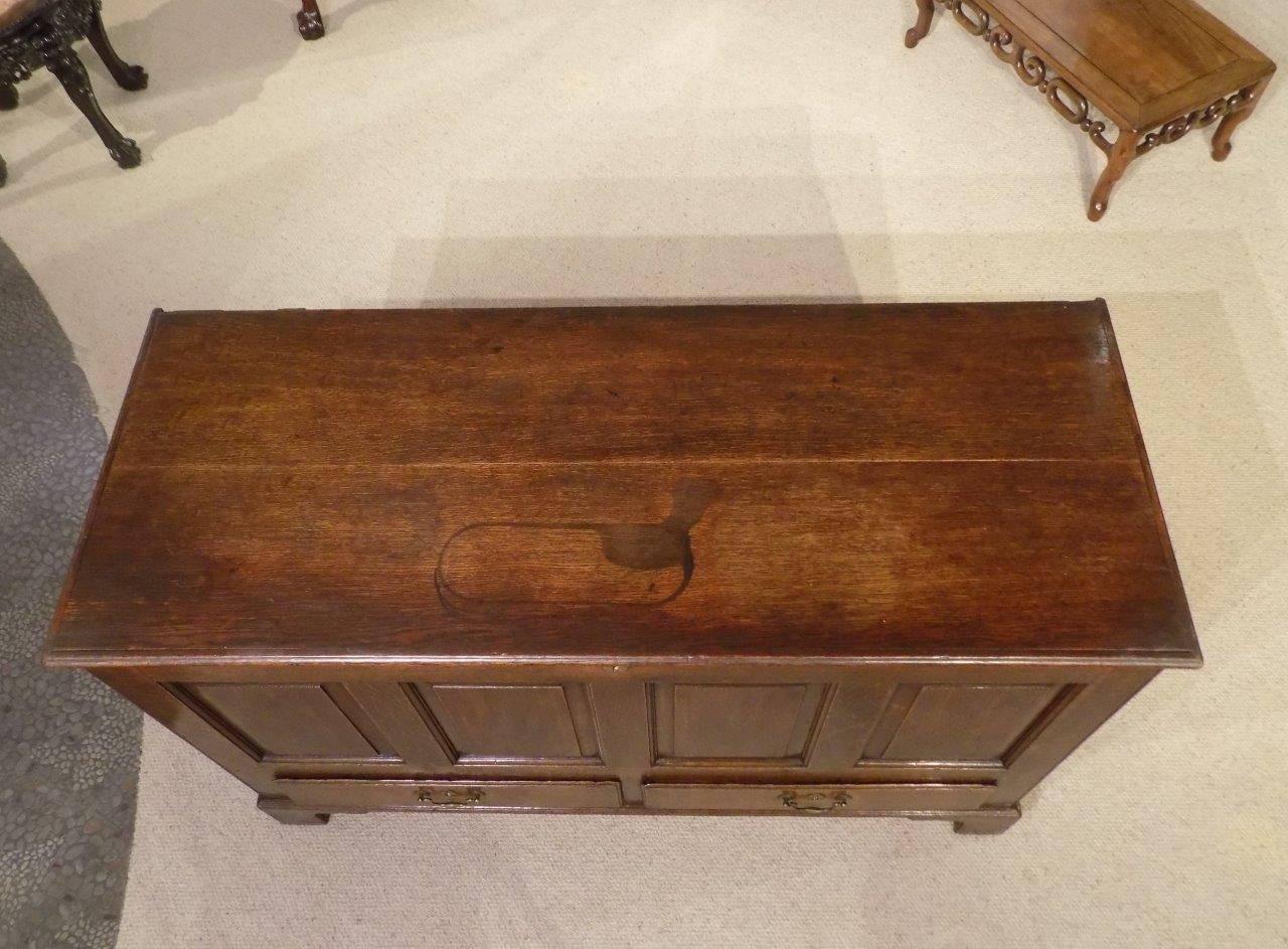 An oak late 18th century English four panel mule chest. Having a two plank oak top opening to reveal storage area, a candle box and two small internal drawers. The front with four fielded oak panels and two rectangular drawers having the original