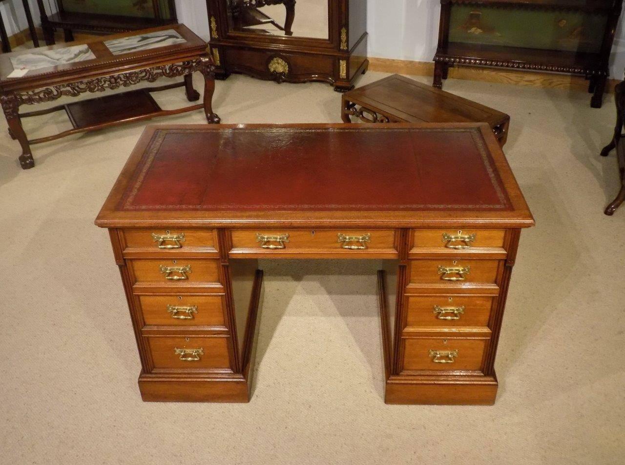 A mahogany Late Victorian Period antique pedestal desk by Hindley & Sons of London. Having a rectangular solid mahogany top with an inset rouge leather writing surface with blind and gilt tooled detail and a moulded edge. With an arrangement of