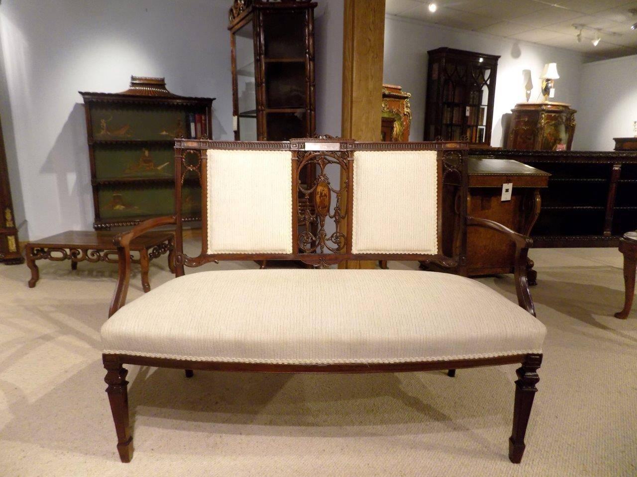 A fine quality mahogany inlaid and carved Edwardian period antique settee. The back with carved mahogany anthemions and a finely carved and pierced fretwork back splat with a marquetry inlaid panel, this is flanked by padded supports and with open