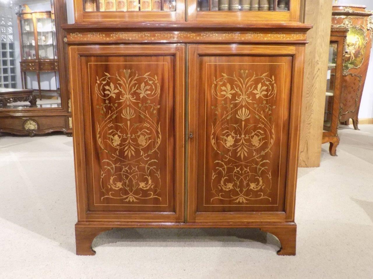 A fine quality marquetry inlaid Edwardian period bookcase by Edwards & Roberts The upper bookcase section has a broken swan neck pediment with carved roundels, pierced fretwork and inlaid detail to the frieze. Having twin solid mahogany doors