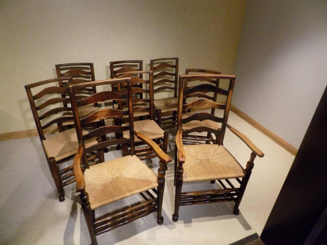 A Good set of eight ash early 19th century ladder back dining chairs with rush seats, comprising of two carver arm chairs with shaped top rails, wavy ladder backs and open arms, supported on turned front supports with triple 