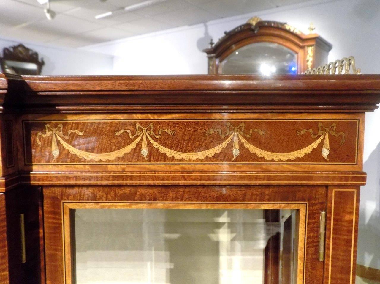 A stunning quality pair of Edwards & Roberts fiddleback mahogany inlaid antique display/china cabinets. Each having a solid mahogany top of breakfront outline and a raised brass gallery with satinwood crossbanded detail. The frieze with a central