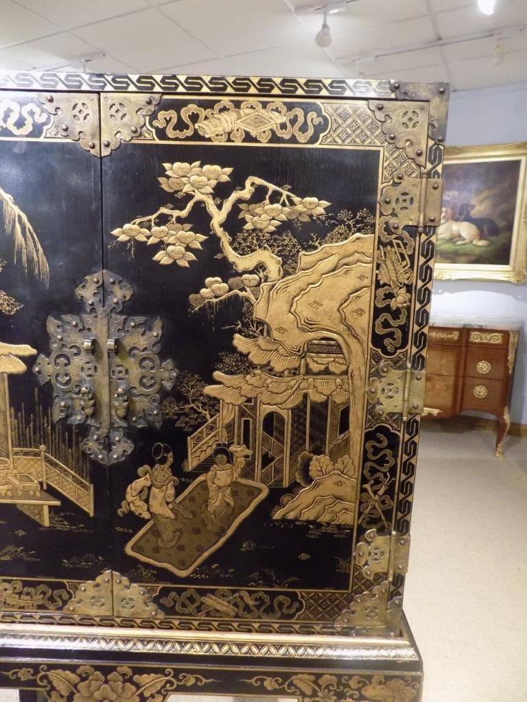 A chinoiserie gold lacquered cocktail cabinet on stand. The upper section with gold lacquered panels to the top, front and sides depicting Oriental landscapes with an engraved brass lock plate and hinges, opening to reveal a shelf and two drawers.