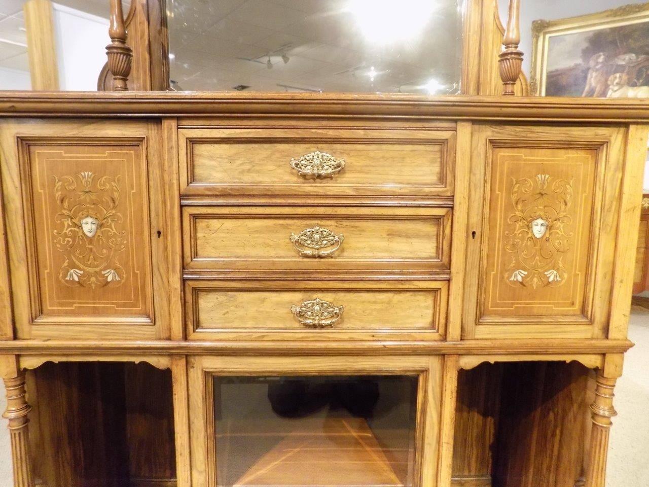 A walnut and marquetry inlaid late Victorian period antique side cabinet. The upper section with a broken swan neck cornice with marquetry inlaid detail moulding above the shaped bevelled mirror and with finely turned column supports. The lower