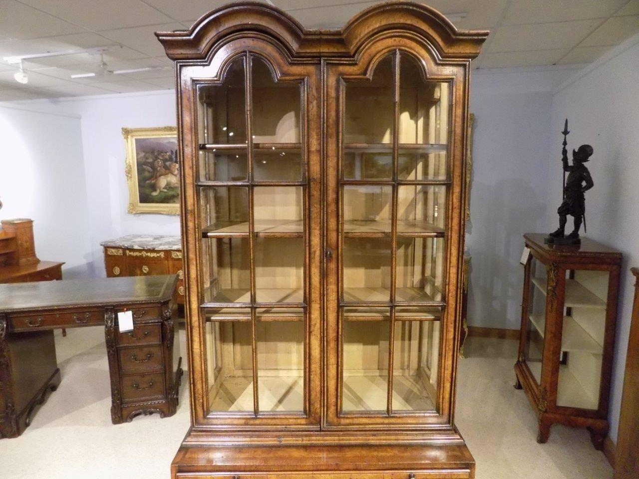 A Queen Anne style double dome cabinet on chest. Having an upper cabinet section with double domed cornice above arched doors with cross grained walnut glazing bars and opening to reveal three adjustable shelves. The lower chest section with a