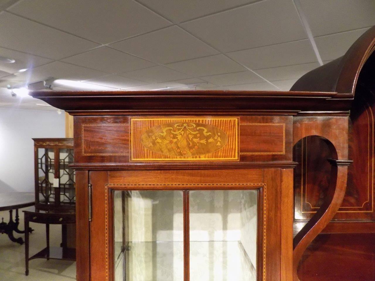 A fine quality mahogany inlaid Edwardian period display cabinet by Shapland and Petter Of Barnstaple. Having a central domed cornice above a panelled and inlaid back, flanked by twin mahogany glazed doors with fine marquetry inlaid panels, opening