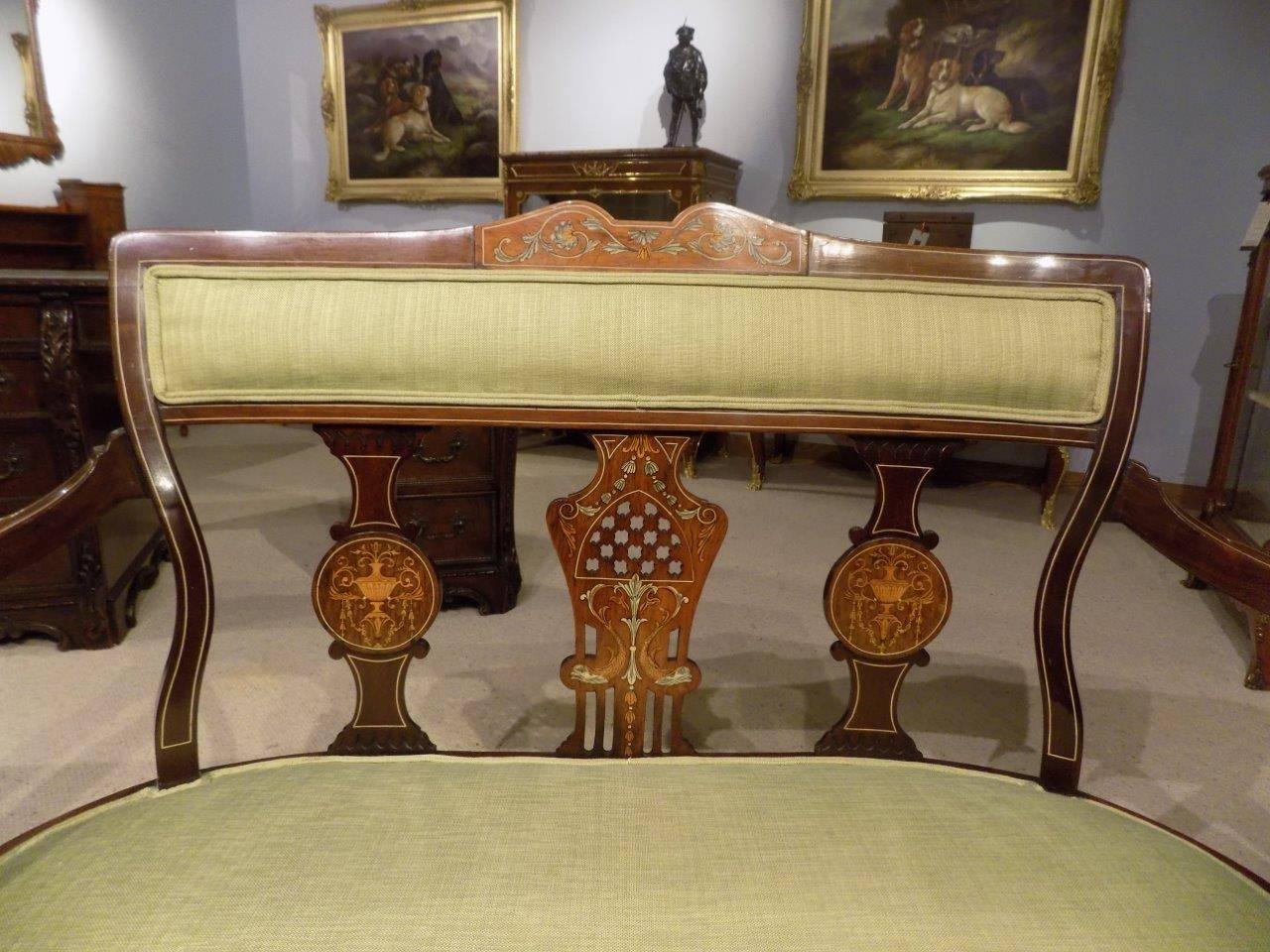A fine quality mahogany inlaid Edwardian period settee. Having a shaped back with a padded support and a central pierced fretwork and marquetry panel, flanked by two supports with marquetry inlaid detail. The padded seat newly re-upholstered in a