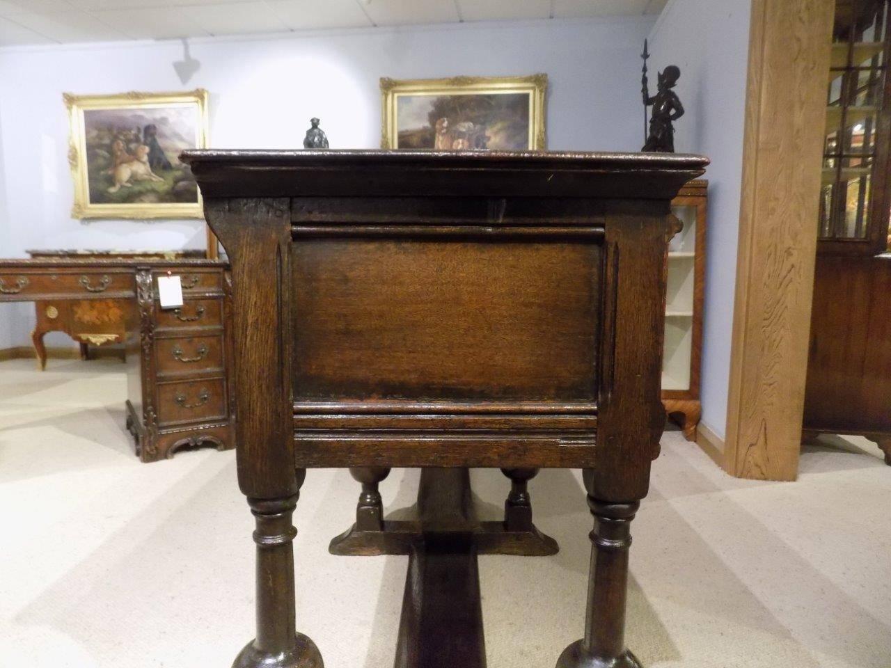 An oak Jacobean Style two-drawer antique dresser base. The rectangular two plank solid oak top above two block fronted drawers with brass drop handles. Supported on six bulbous turned legs with sledge supports and united by a central plank