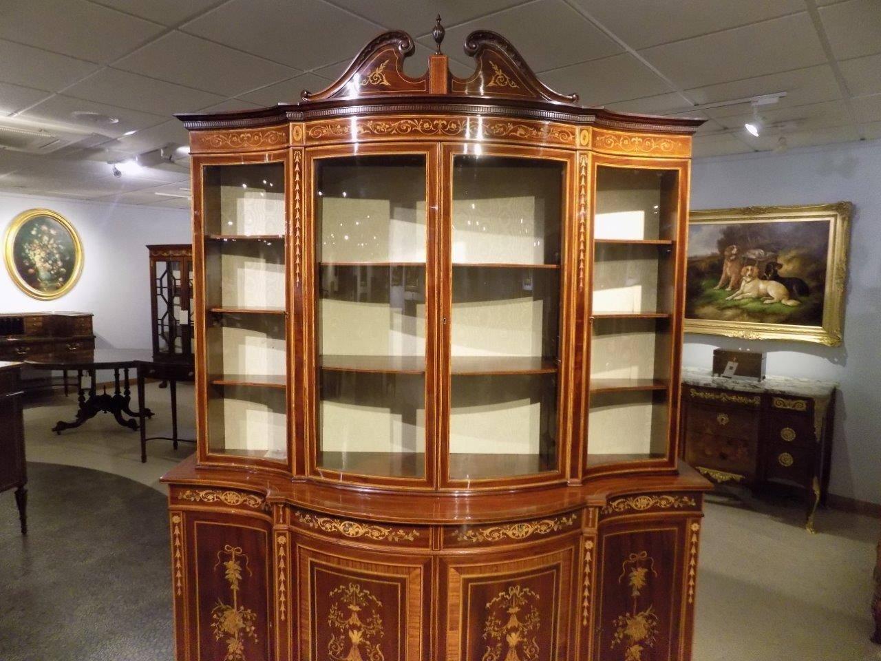An exhibition quality serpentine mahogany display cabinet by Edwards and Roberts of London. The upper section with a serpentine outline and a broken swan neck pediment surmounted by a mahogany turned finial. Having central bow front doors flanked by
