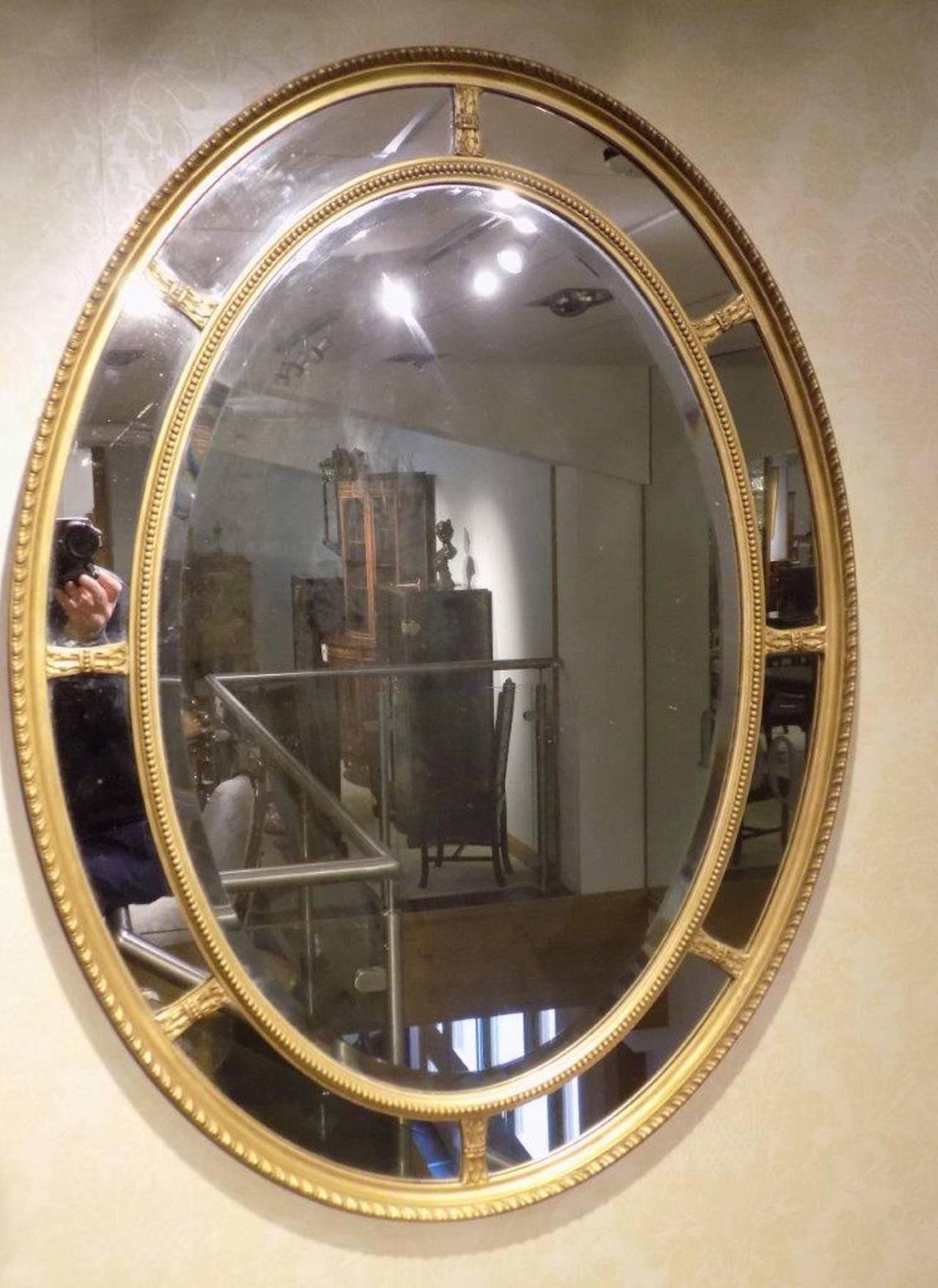 A gilt George III style oval margin mirror. Housed in a carved gilt-wood and gesso frame with a central bevelled mirror, flanked by smaller margin mirrors with a gadrooned carved border, English, circa 1900

Dimensions: 39