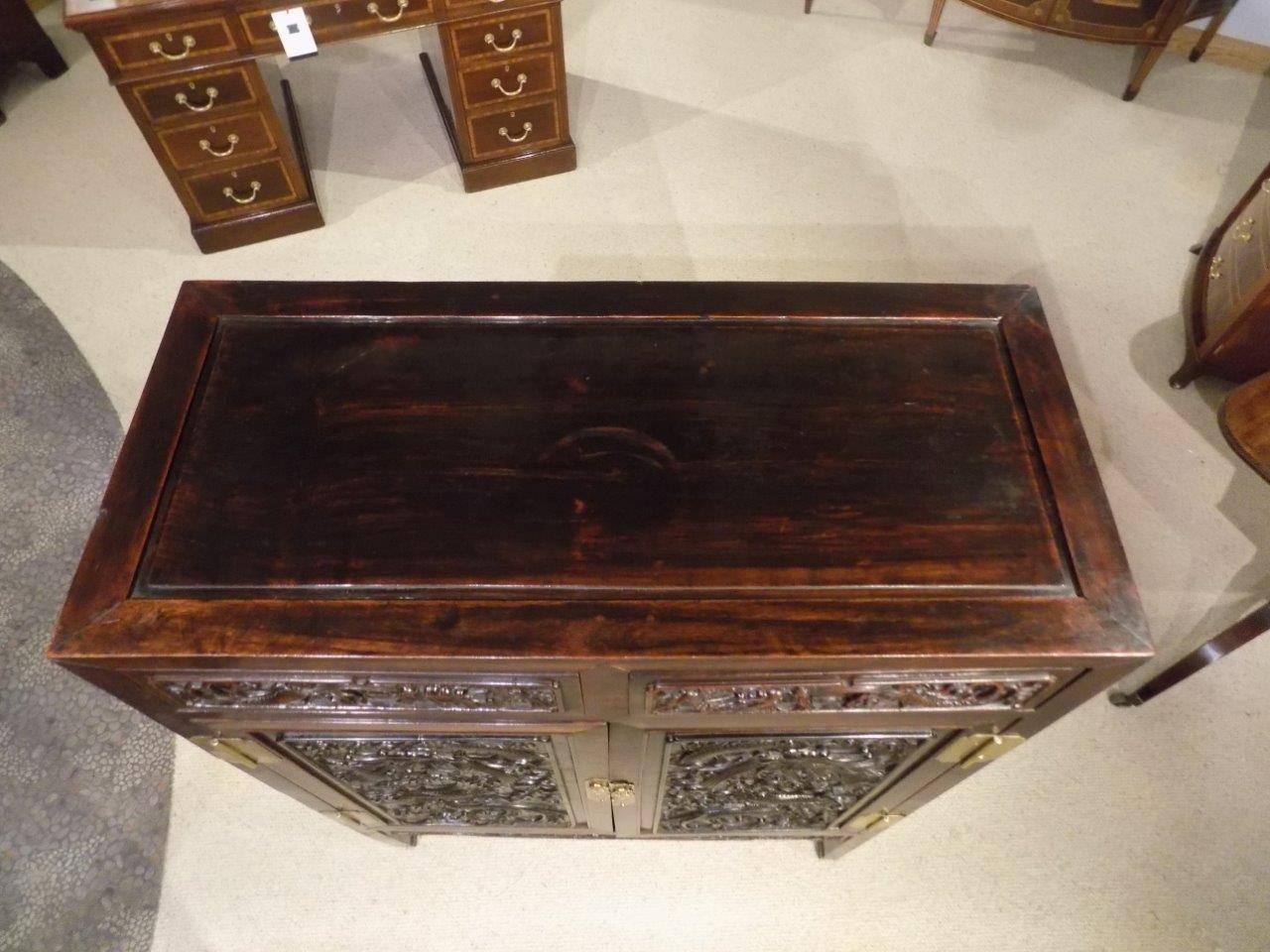 A 19th century finely carved Chinese hardwood cabinet. The panelled top above two drawers and two cupboards, each with finely carved detail depicting dragons, opening to reveal a shelved interior with carved panelled ends, Chinese, circa