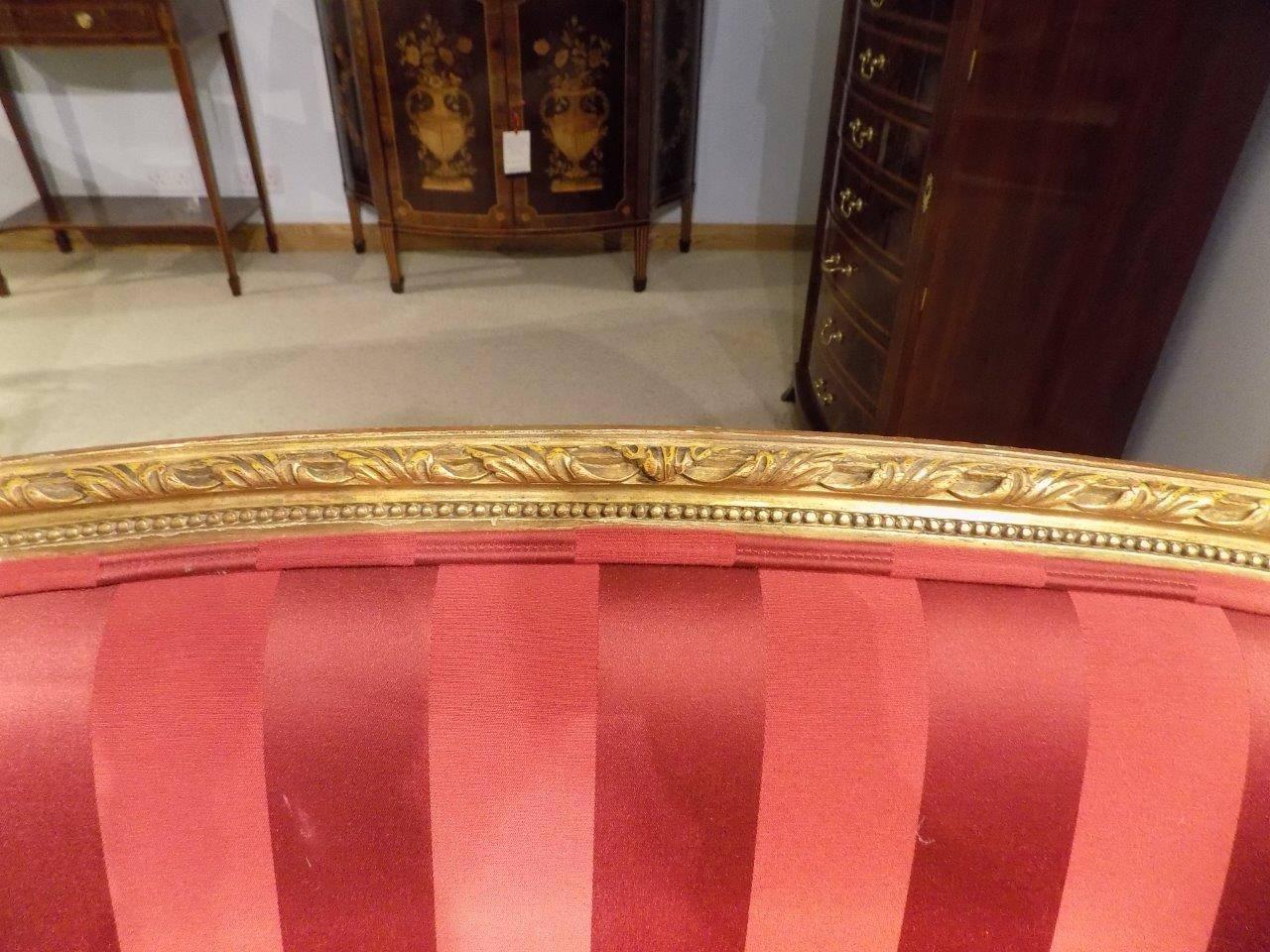 A carved giltwood antique French canapé/settee. Having a carved giltwood frame with acanthus detail to the arms and upholstered in a striped red silk. Supported on turned and fluted supports, French, circa 1900.

Dimensions: 33