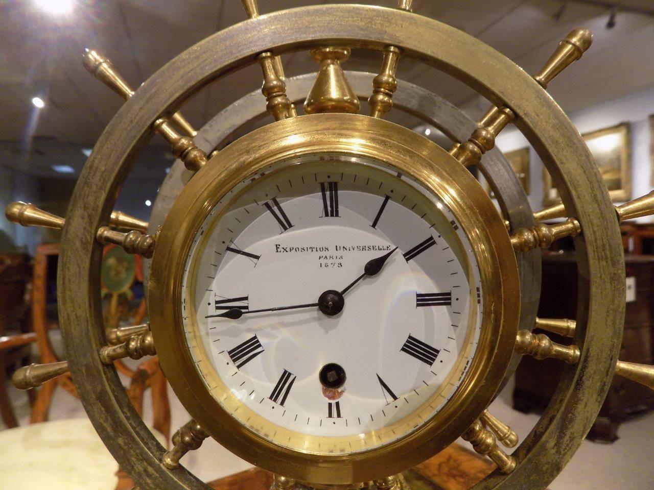 A rare novelty nautical revolving ships wheel desk clock or barometer. Each side is modelled as a steel and brass ships wheel with one side has an aneroid barometer and the opposite side has a clock. Each with enamelled dials and titled 