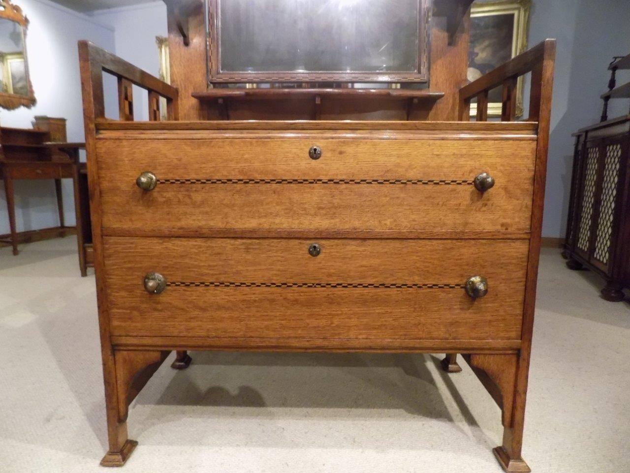 An oak Arts & Crafts period shapland and petter dressing table. The upper section with a rectangular bevelled mirror with chequer band inlay, marquetry inlaid supports and shaped shelves. The open ends having further marquetry inlaid panels. The