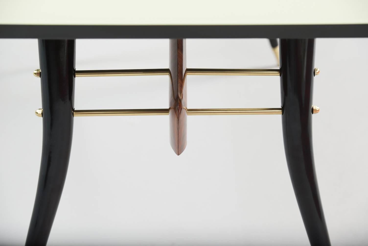 Rosewood and ebonized wood dining table, brass fittings and lacquered glass top.